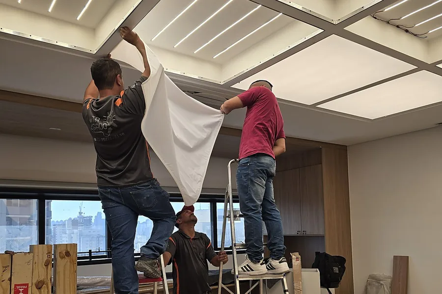Dois instaladores esticando a lona tensionada sobre o nicho no gesso